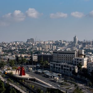 An urban area surrounded by greenery buildings and roads under sunlight and a cloudy sky